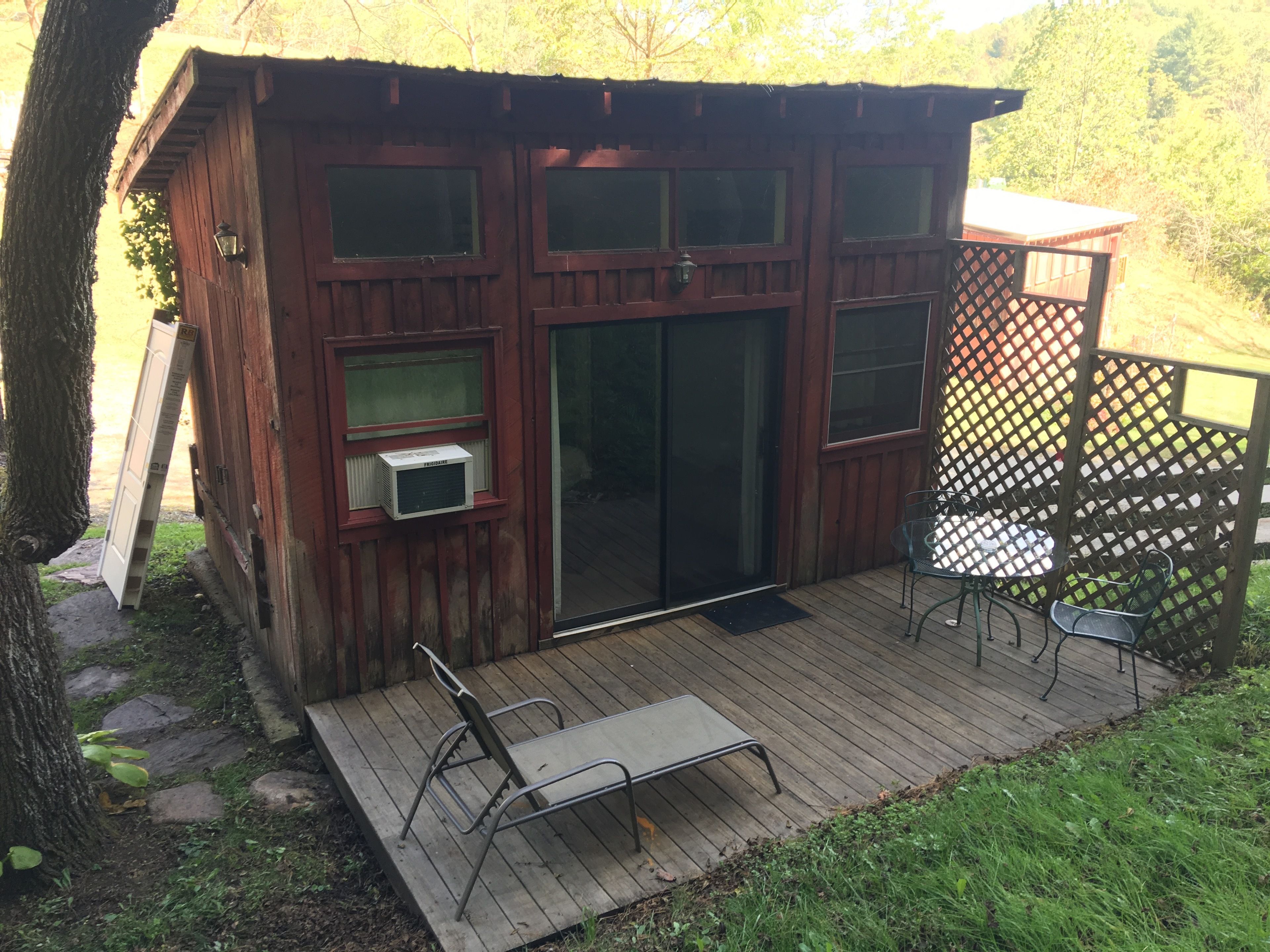 Eine Holzhütte mit einer Terrasse, einer Schiebetür und einem kleinen Tisch mit Stühlen im Freien.