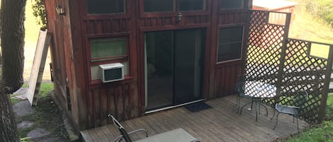 Eine Holzhütte mit einer Terrasse, einer Schiebetür und einem kleinen Tisch mit Stühlen im Freien.