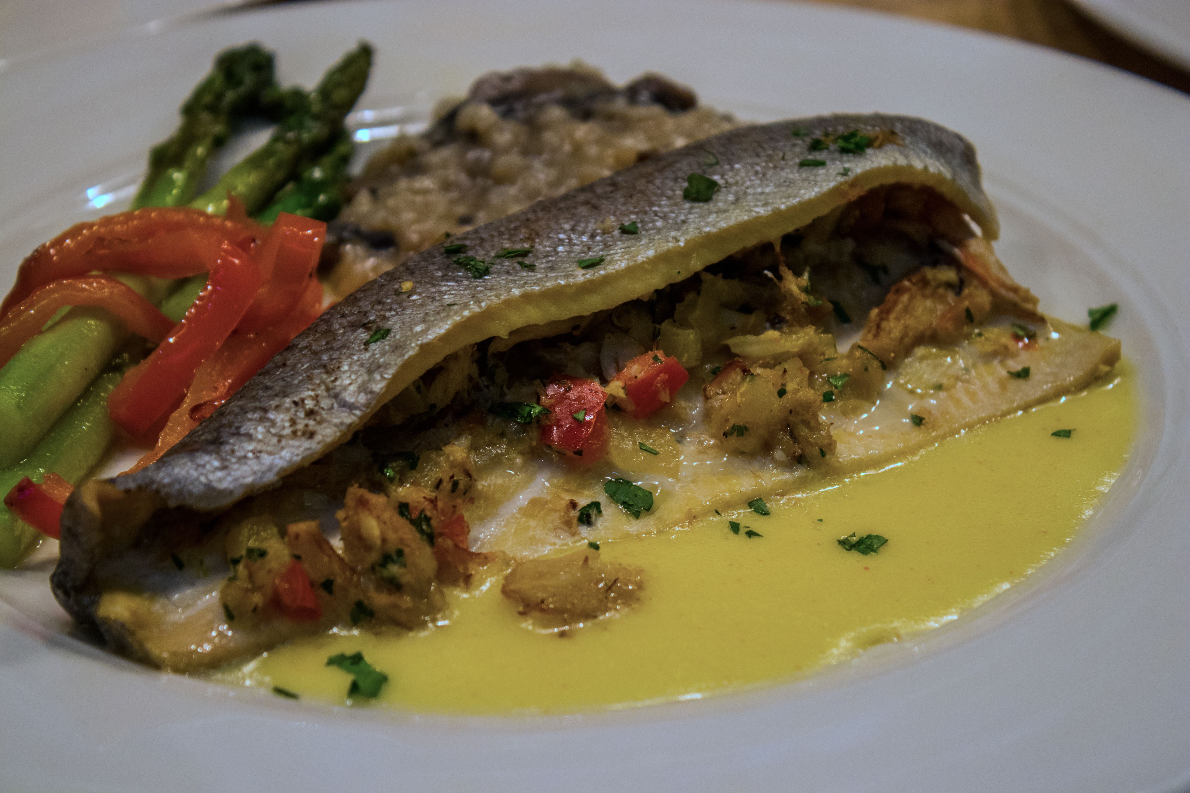 Een bord met een visfilet, asperges en paprika.