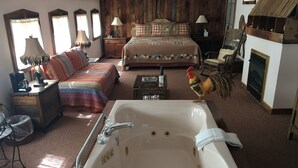 A spacious bedroom with a large bed, a sitting area with a chair and a table, a bathtub, and a wooden floor. - River House Inn (Grassy Creek)