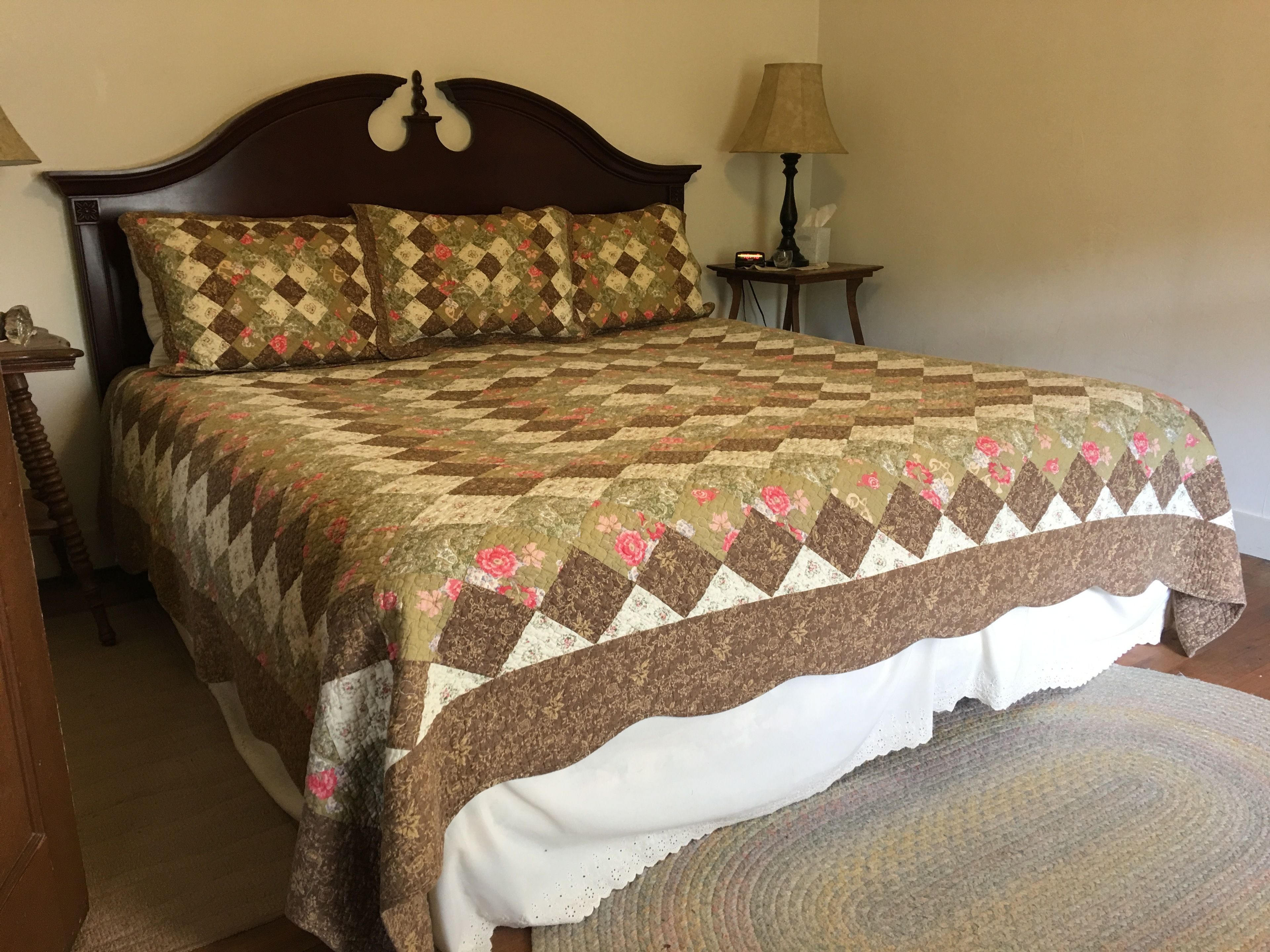 A bed with a quilt, a nightstand, a lamp, and a rug.