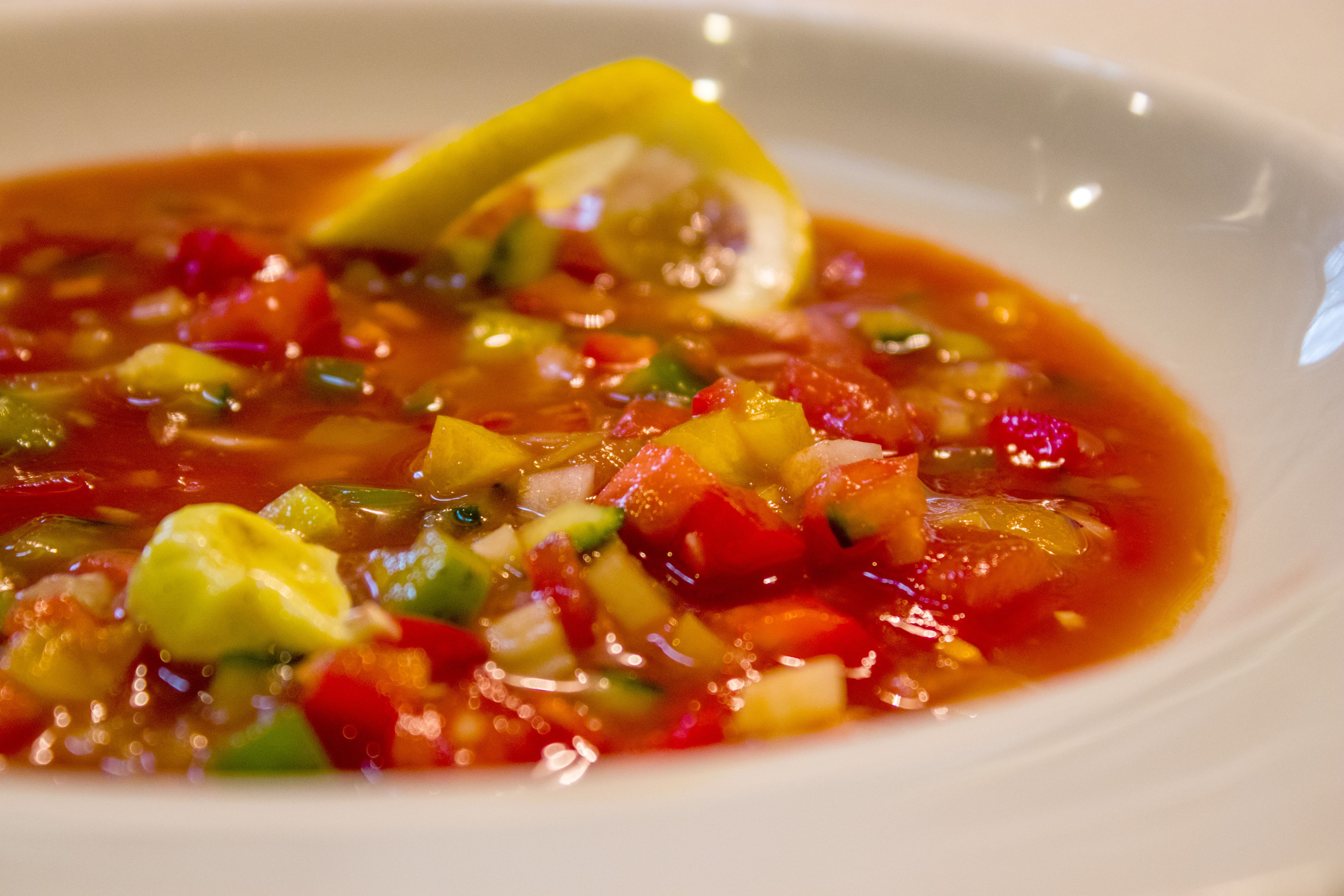 En skål suppe med forskellige grøntsager og et stykke citron ved siden af.