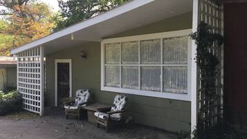 A small building with a porch, two wooden chairs, a table, and a window with lace curtains.