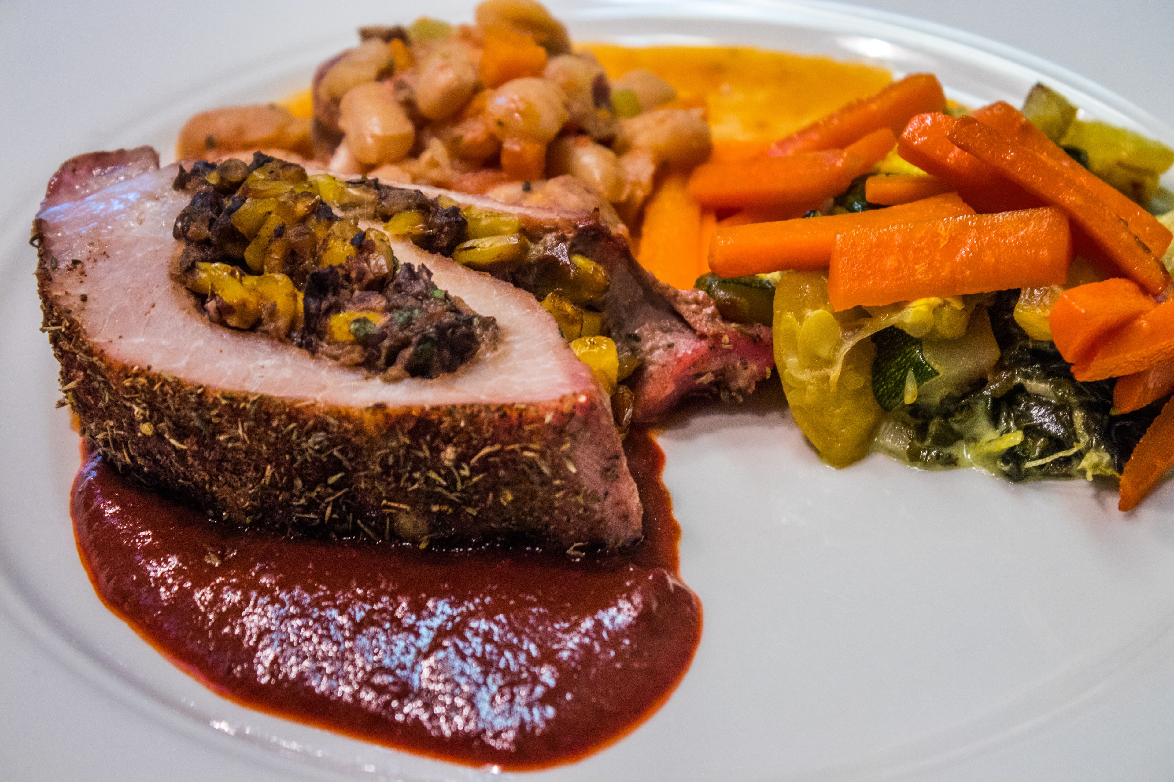 A plate with sliced meat, carrots, and a red sauce.