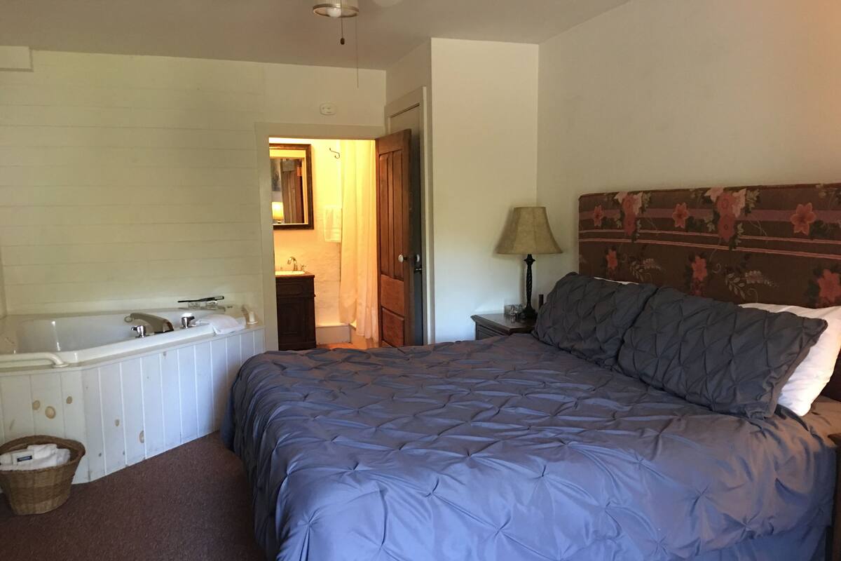 Un dormitorio con una cama grande, un baño con bañera y un cabecero de madera.