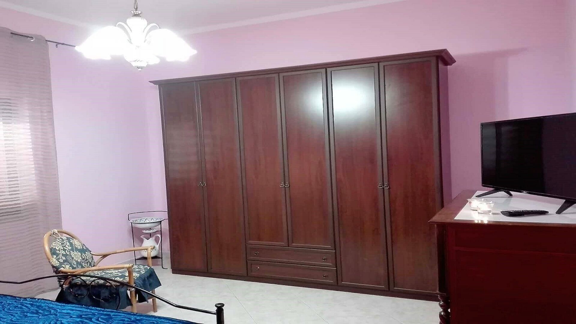 A bedroom with a wardrobe, a television, and a chair.