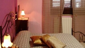 Een slaapkamer met een bed, nachtkastje, lamp en een raam met zonwering.