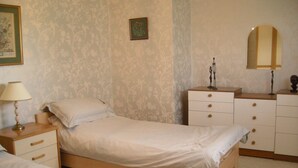 Een slaapkamer met een enkel bed, een nachtkastje met een lamp, een dressoir met laden en een spiegel aan de muur.