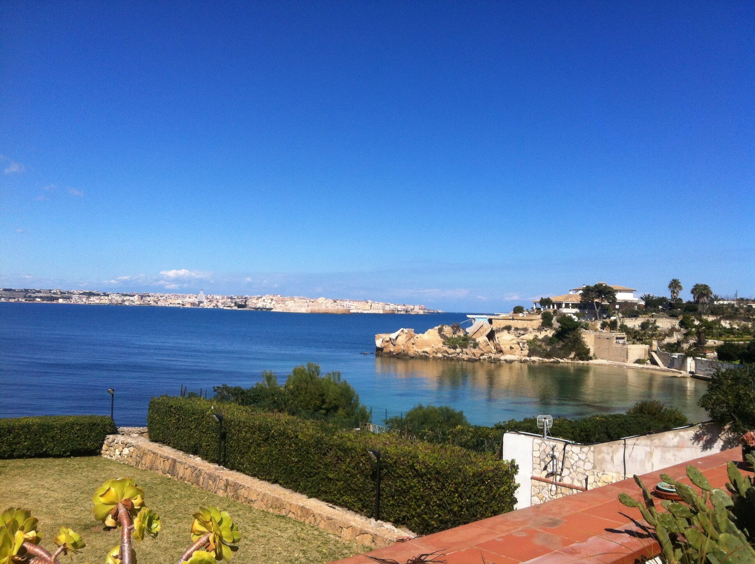 A coastal view with a clear sky, a body of water, and a distant cityscape.