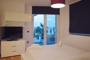 Een slaapkamer met een televisie, een bed met handdoeken, een glazen schuifdeur naar een balkon en een plafondlamp.