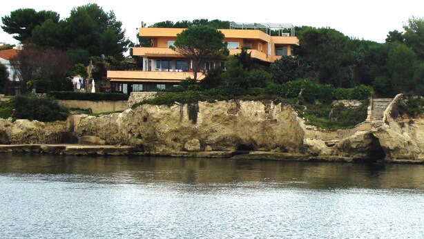 A coastal property with a modern yellow building, a stone retaining wall, and a staircase leading up to the building. - design villa on the sea with a splendid view of the Gulf of Syracuse (Siracusa)