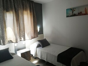 Une chambre d’hôtel avec deux lits simples, une table de chevet, une petite table et un tableau représentant un paysage urbain accroché au mur.