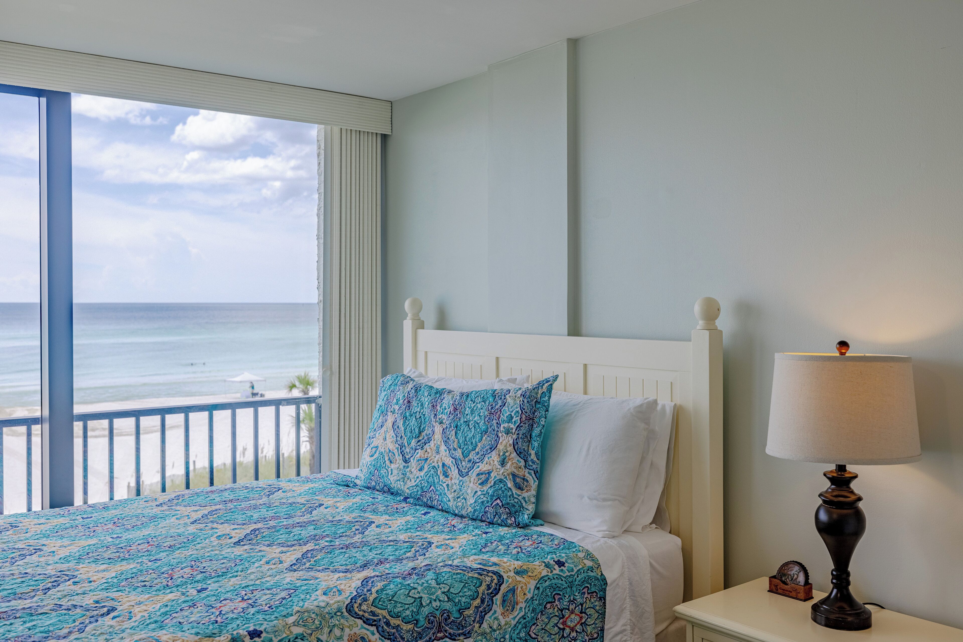 A bedroom with a bed, a nightstand, a lamp, and a view of the ocean.