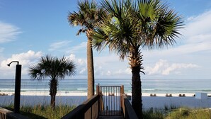 Ein Strand mit Palmen, einer Holzpromenade und Liegestühlen.