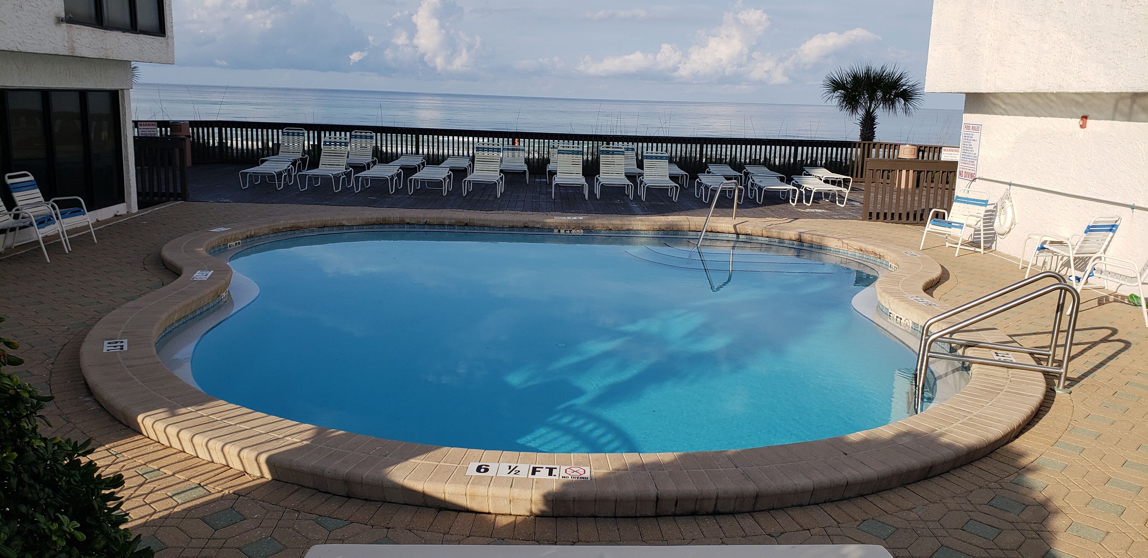 Une piscine avec une zone aménagée, des chaises longues et une vue sur l’océan.