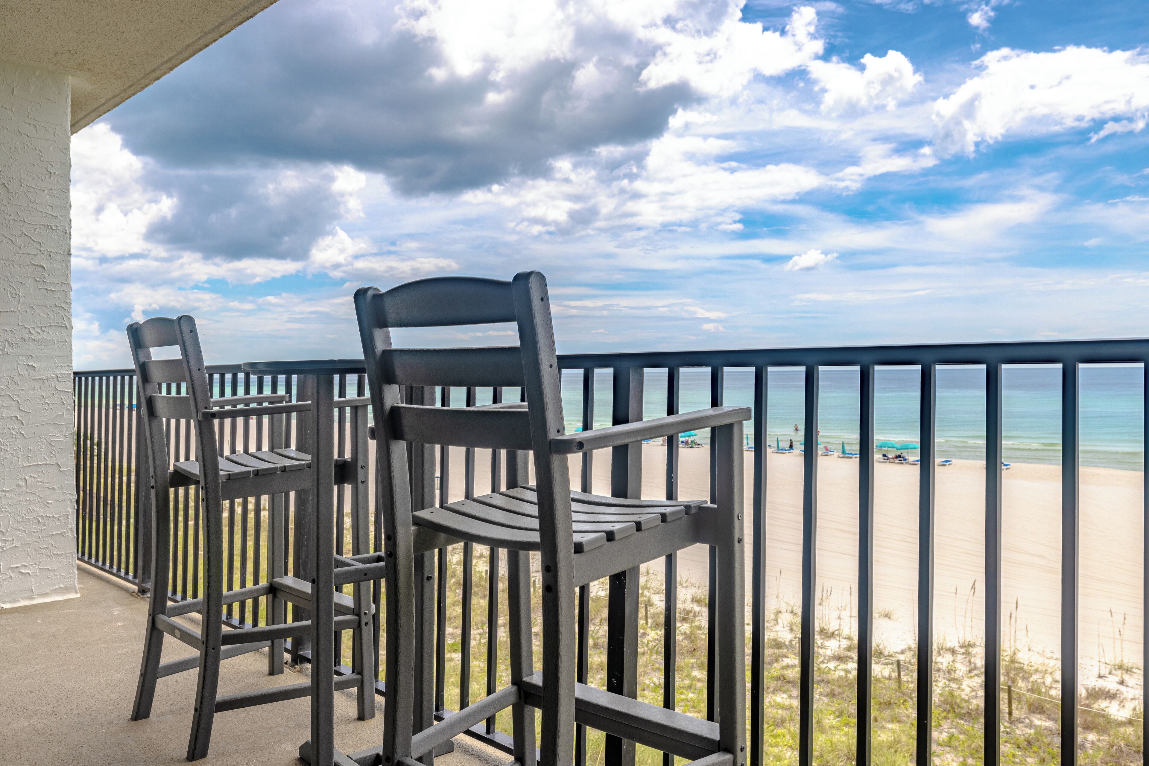 A balcony with two chairs overlooking a beach.