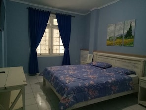 A bedroom with a bed, a nightstand, a desk, and a window with curtains.