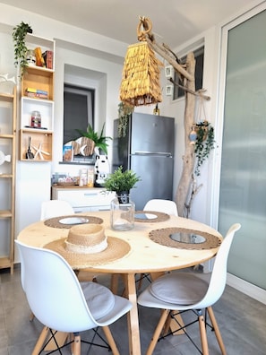 Une table de salle à manger ronde, avec des chaises blanches, un centre de table en fibres tressées et un luminaire suspendu.