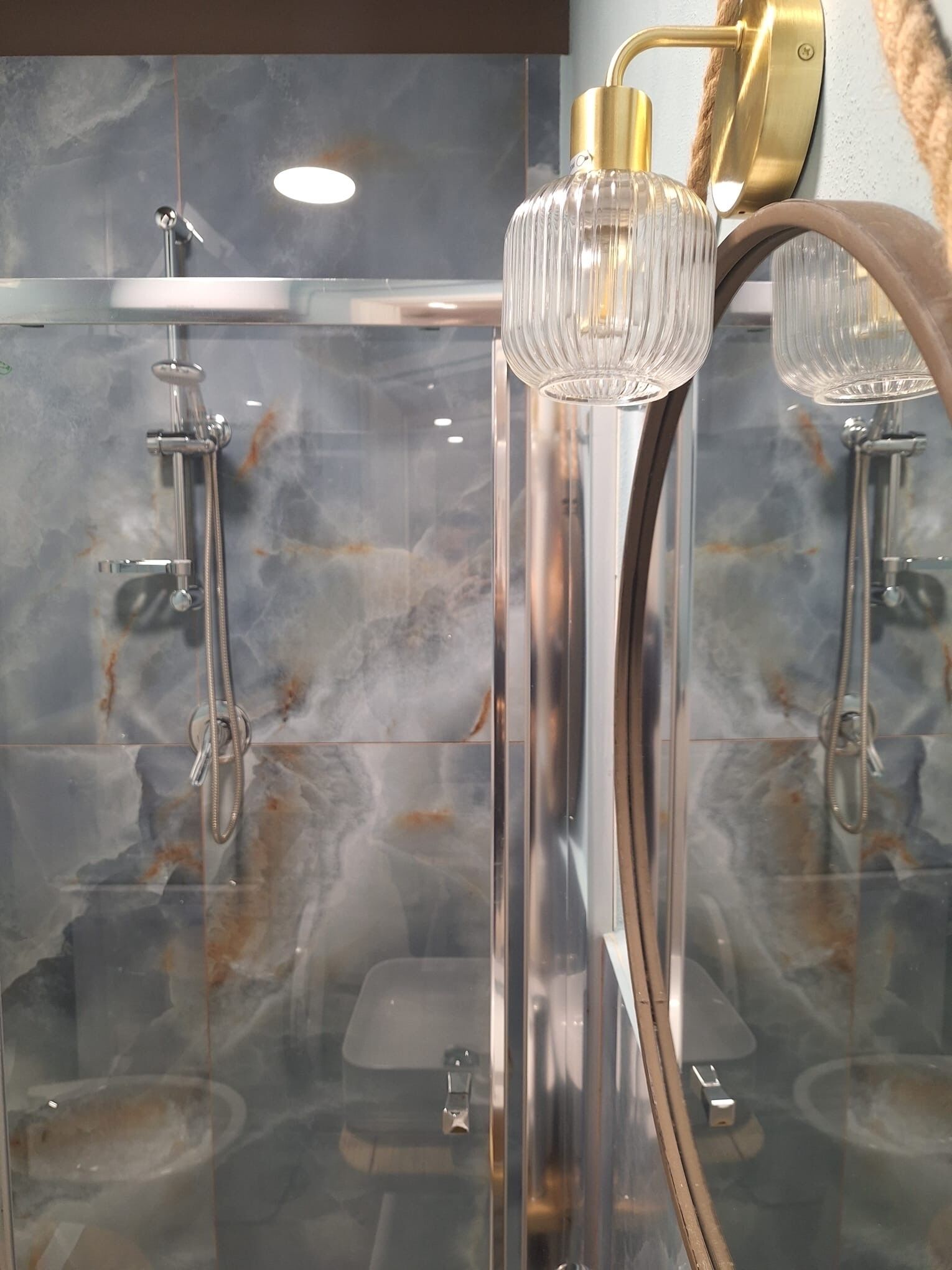 A modern bathroom with a glass shower enclosure, a gold faucet, and a marble backsplash.
