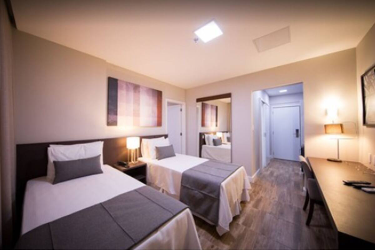 A hotel room with two beds, a desk, and a dining area.