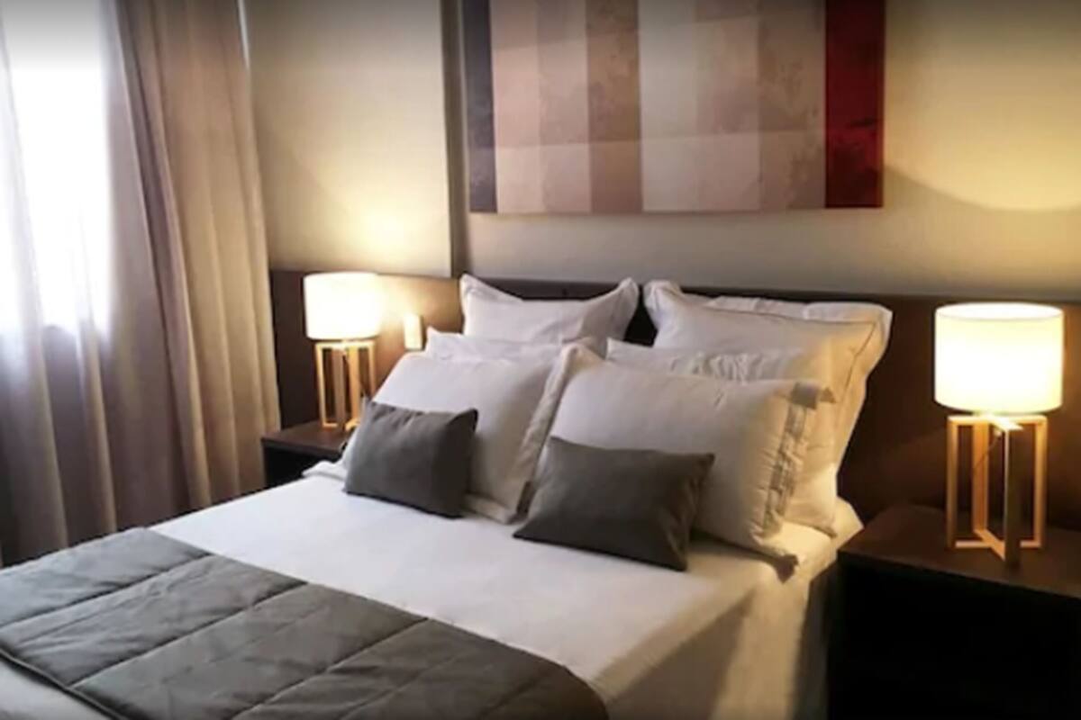A hotel room with a neatly made bed, two bedside lamps, and a large abstract painting on the wall.