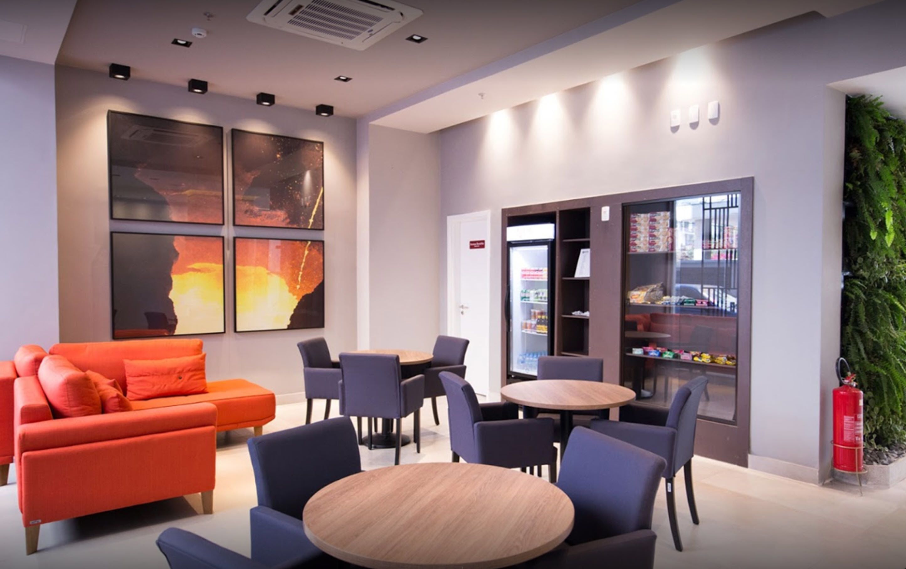 A modern lounge area with a sofa, chairs, a round table, and a refrigerator stocked with snacks.
