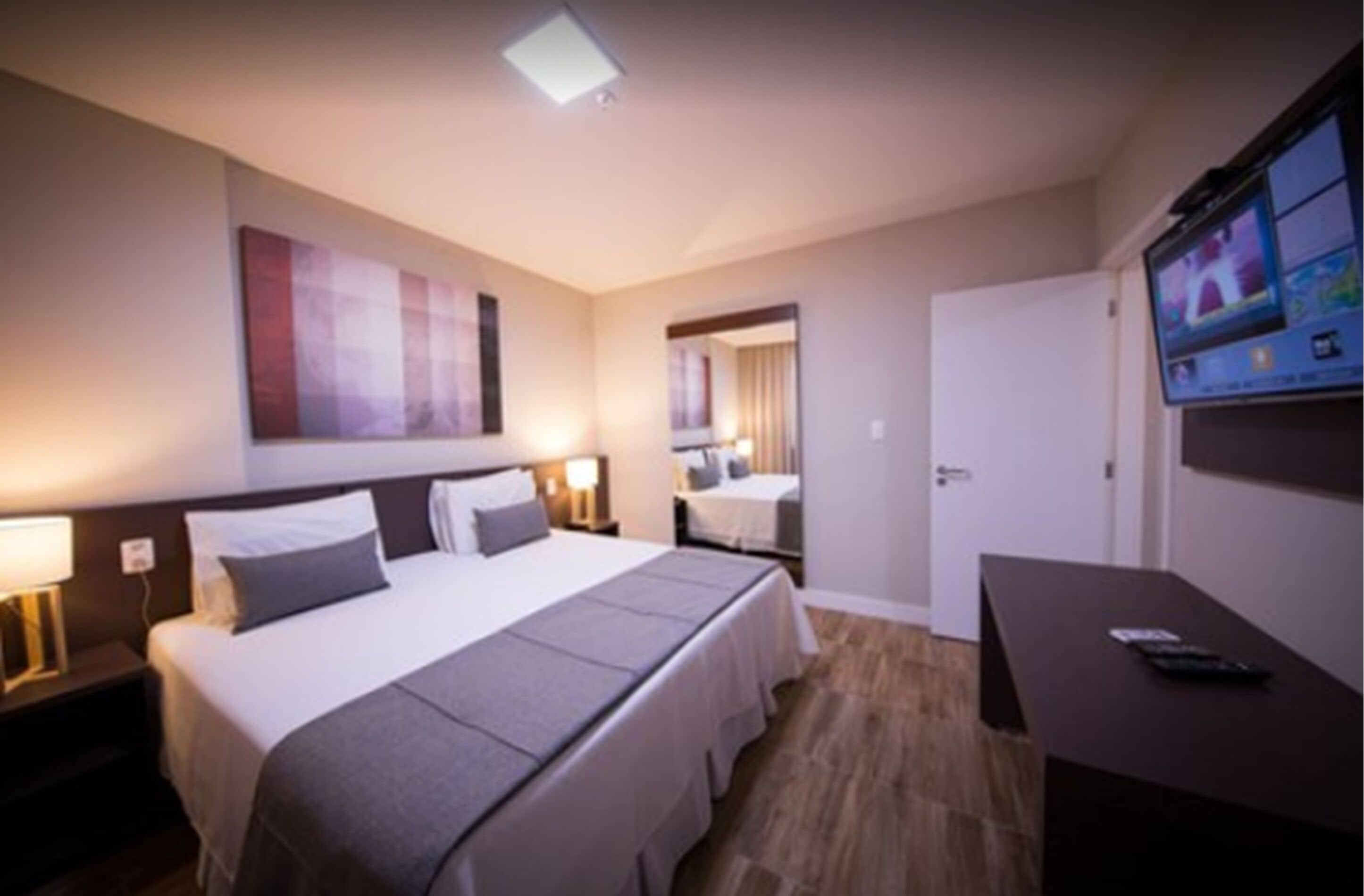 Una habitación de hotel con una cama grande, un escritorio, un televisor y un espejo.