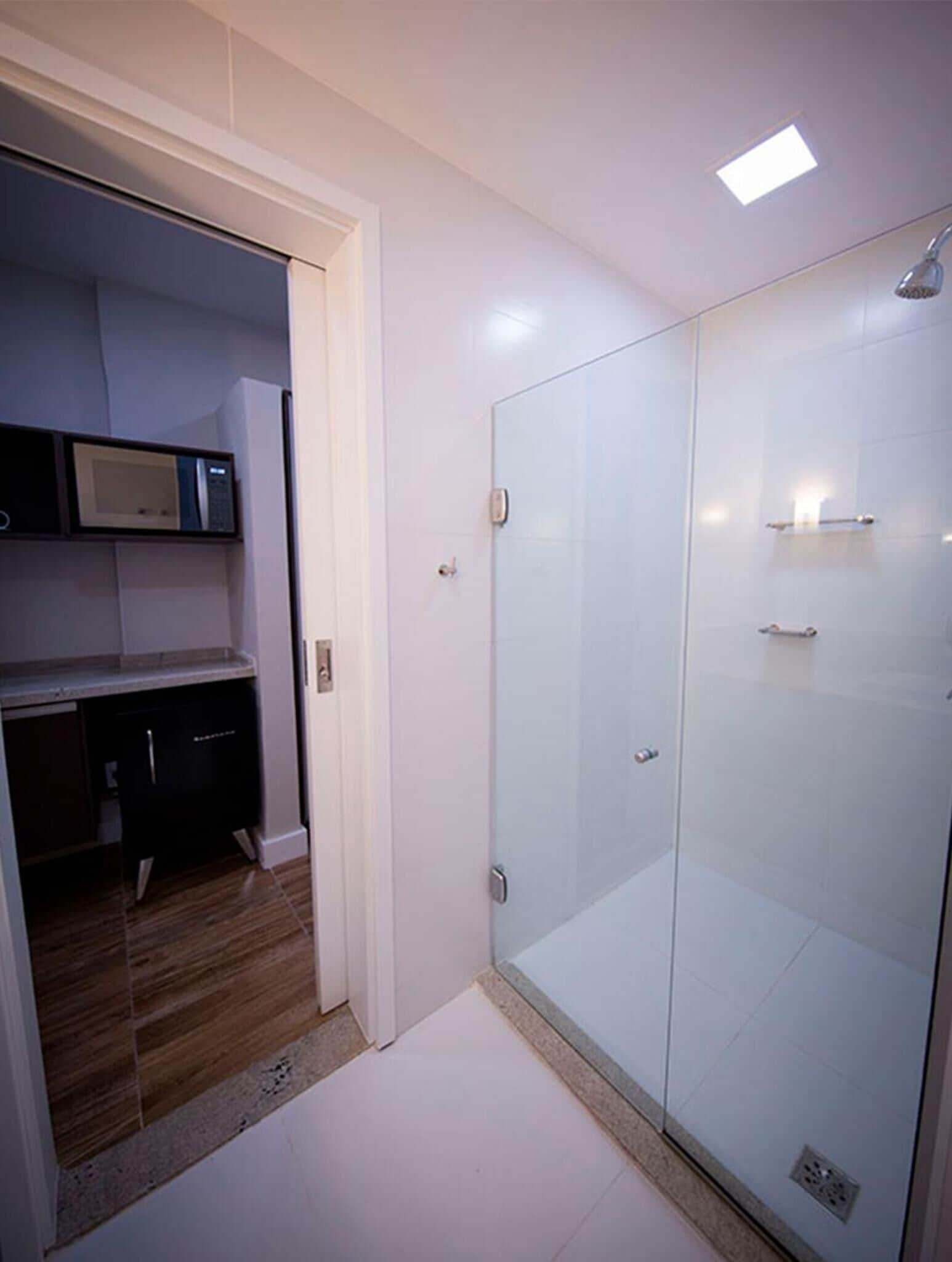 A modern bathroom with a glass shower enclosure, a built-in microwave, and a small kitchen area.