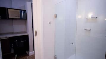 A modern bathroom with a glass shower enclosure, a built-in microwave, and a small kitchen area.