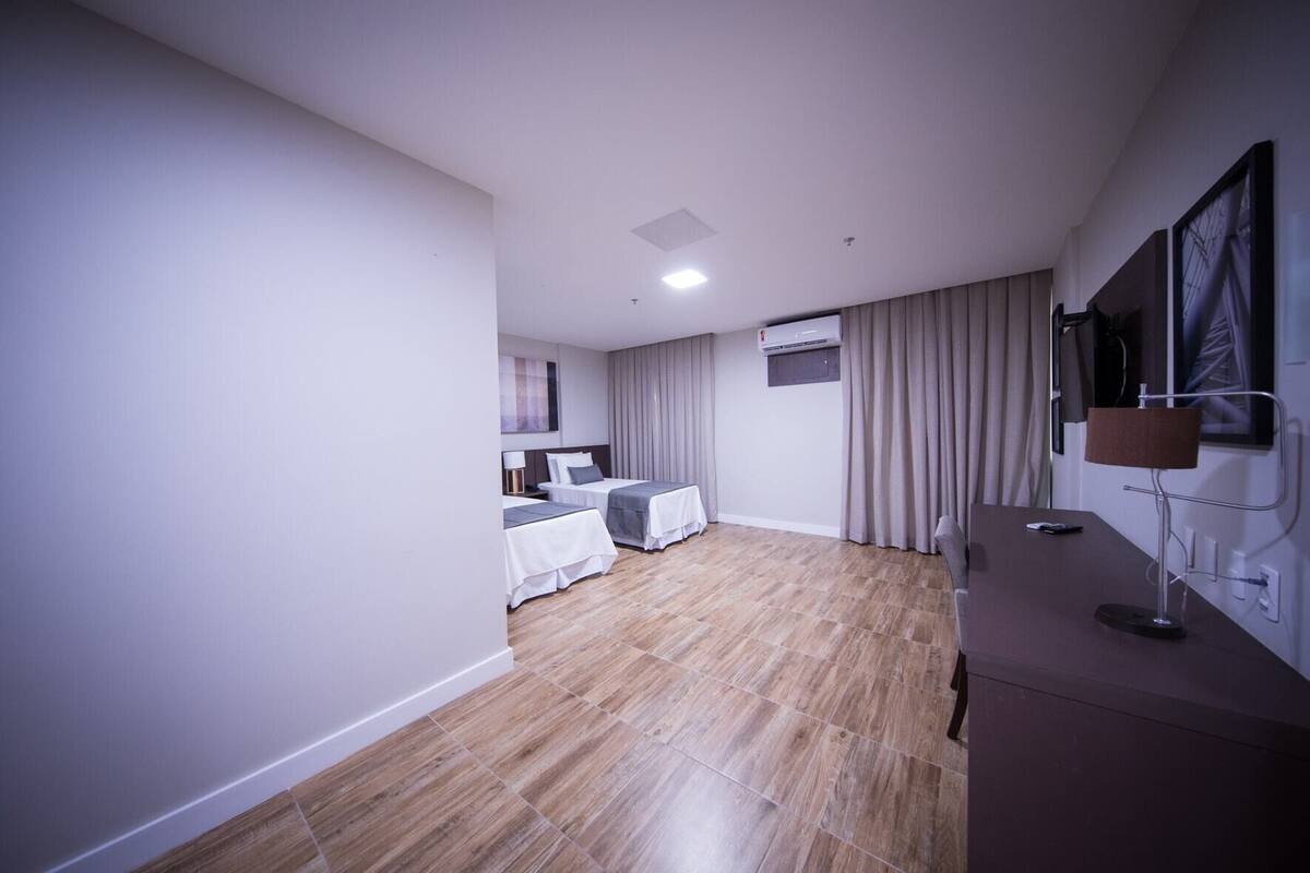 A modern hotel room with a wooden floor, two beds, a TV mounted on the wall, and a desk with a lamp.