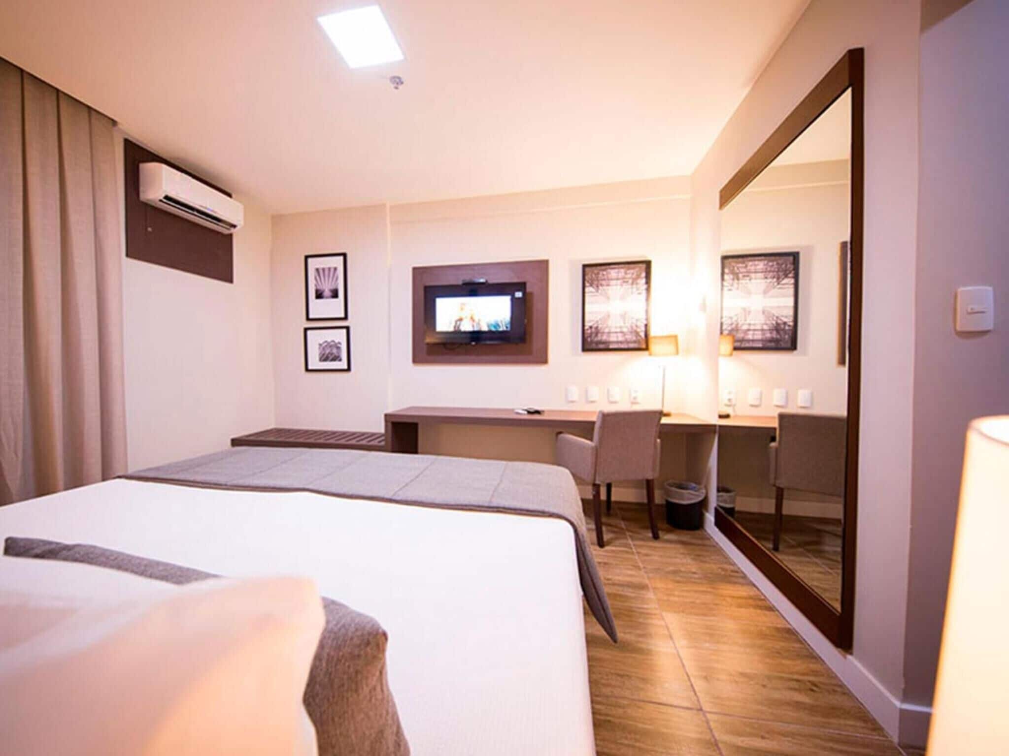 A hotel room with a bed, desk, chair, TV, and artwork on the walls.