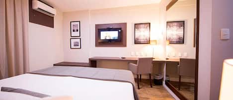 A hotel room with a bed, desk, chair, TV, and artwork on the walls.