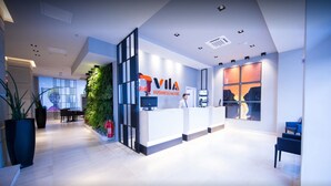 Zona de recepción de un hotel moderno para negocios, con mostrador, un ventanal con vistas a la ciudad y un jardín vertical verde.