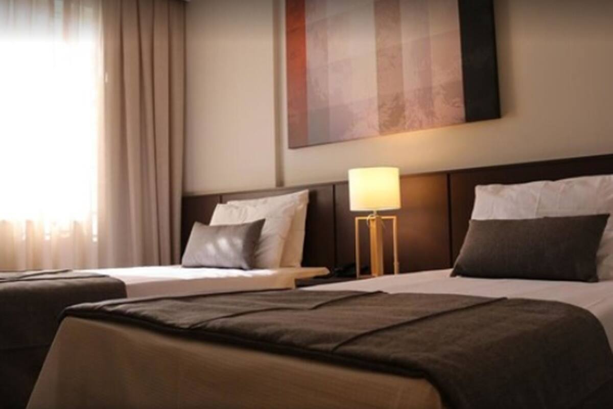 A hotel room with two beds, a nightstand with a lamp, and a large abstract painting on the wall.