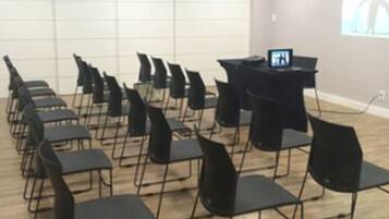 A conference room with rows of black chairs, a podium, and a screen displaying a presentation.