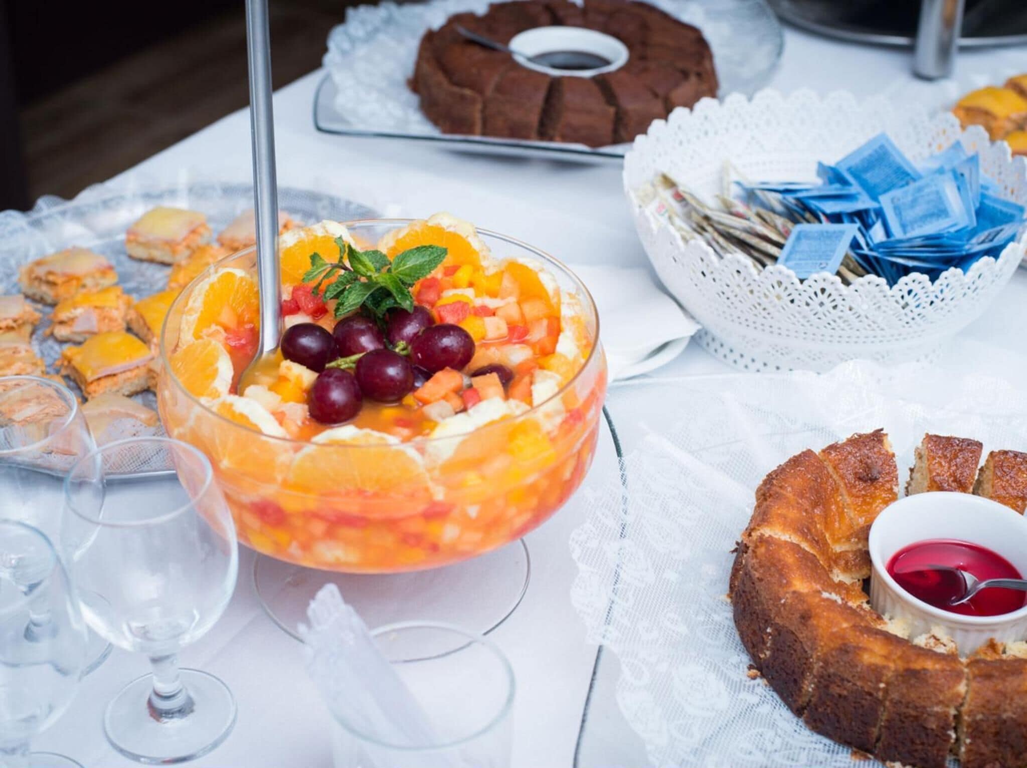 Une table sur laquelle on trouve divers aliments, notamment un saladier de fruits, un gâteau en forme de couronne et un petit bol de confiture.