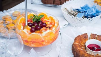 Une table sur laquelle on trouve divers aliments, notamment un saladier de fruits, un gâteau en forme de couronne et un petit bol de confiture.
