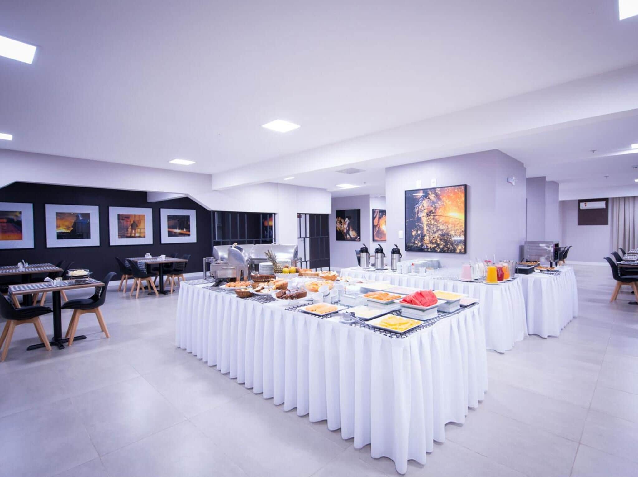 A modern conference room with white tables, chairs, and a buffet setup.