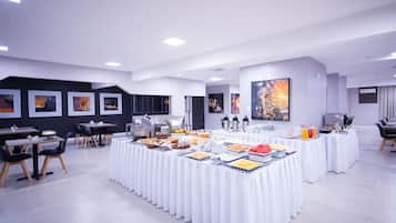 A modern conference room with white tables, chairs, and a buffet setup.