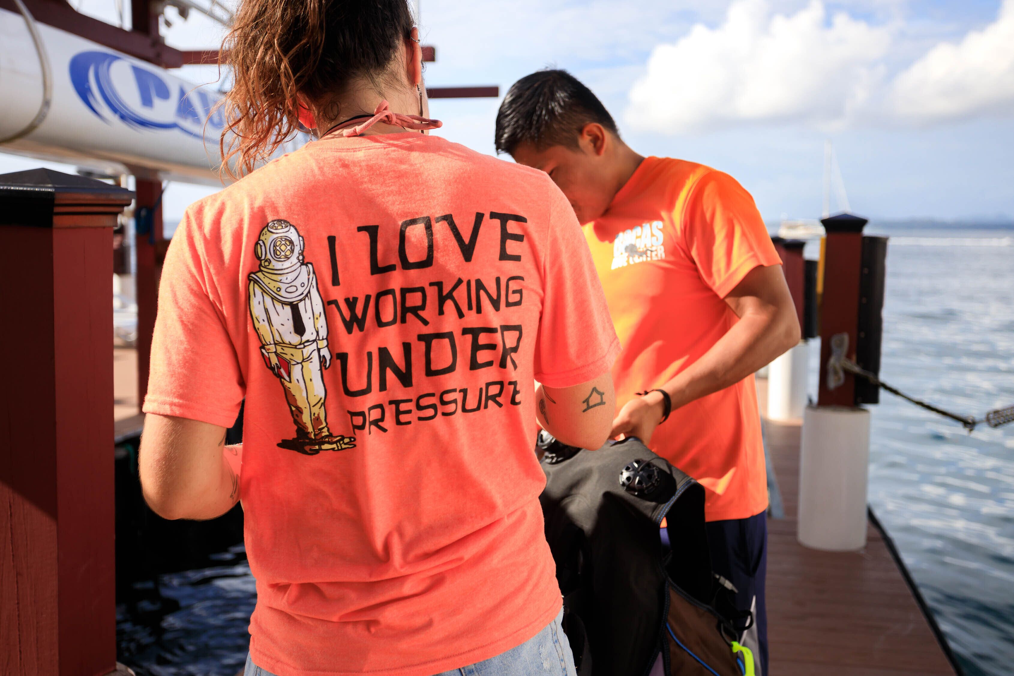 Two people on a boat wearing matching orange shirts with a graphic and text on the back.