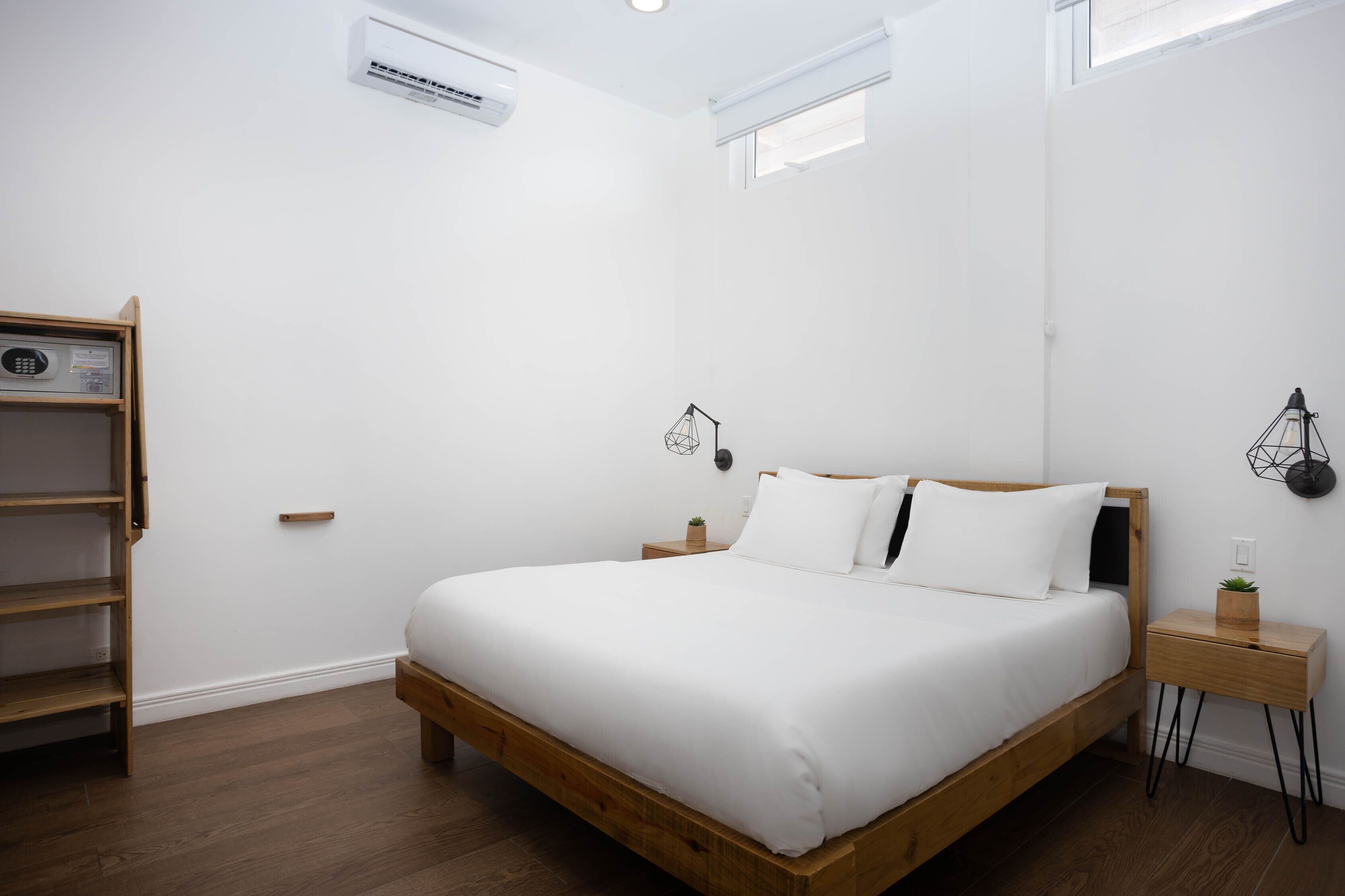 Un dormitorio minimalista con cama de madera, paredes blancas y estante empotrado.