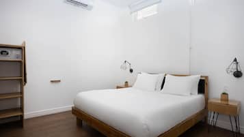 Un dormitorio minimalista con cama de madera, paredes blancas y estante empotrado.