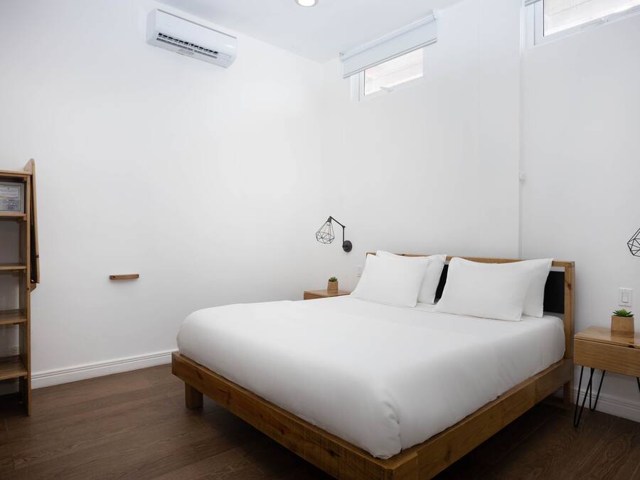 Un dormitorio minimalista con cama de madera, paredes blancas y estante empotrado.