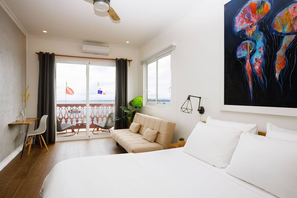 Ein modernes Hotelzimmer mit einem Bett, einer Couch, einem Balkon mit Blick und einem großen abstrakten Gemälde an der Wand.