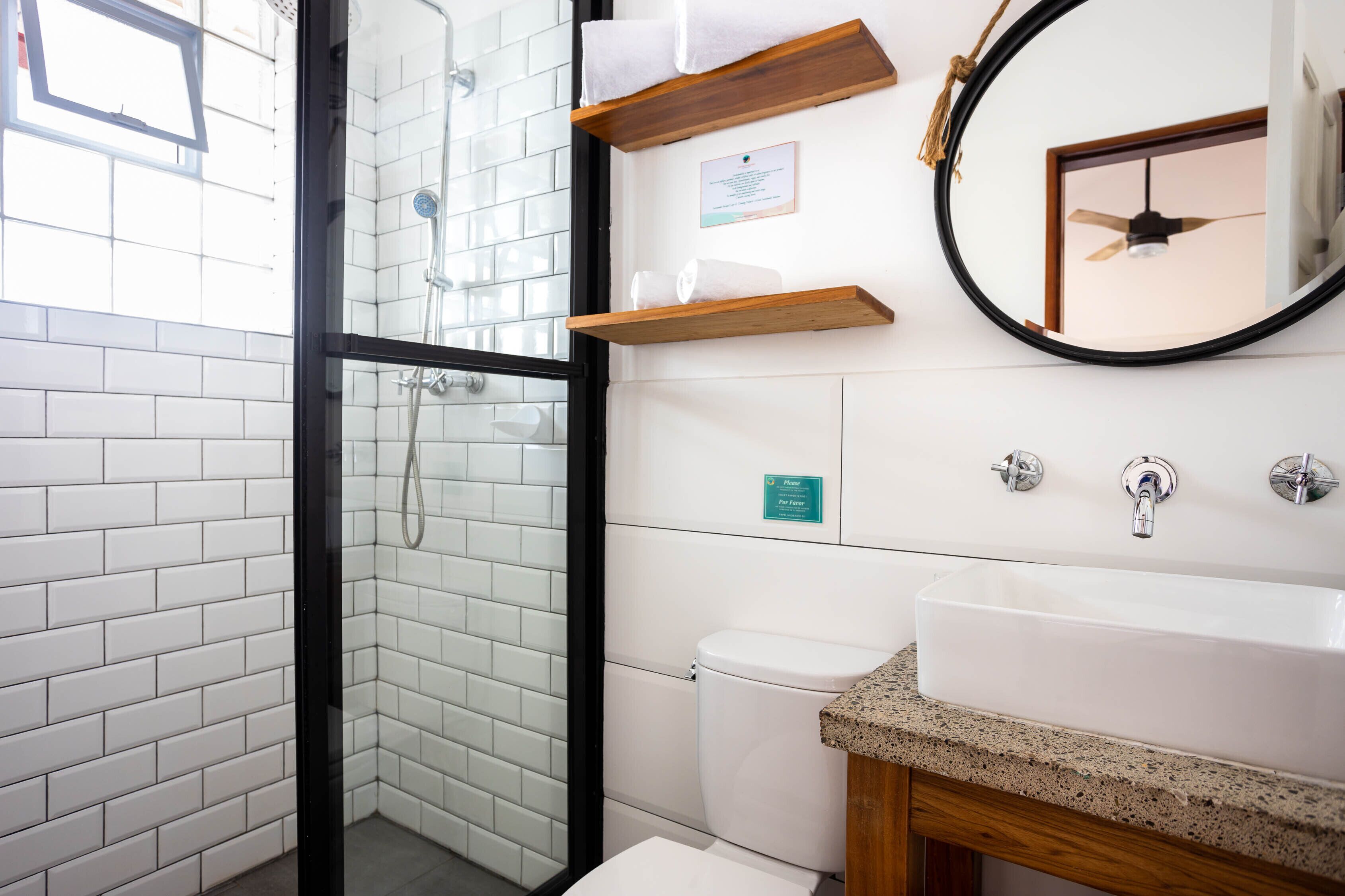 A modern bathroom with a glass-enclosed shower, a white sink with a granite countertop, and wooden shelves above the sink.