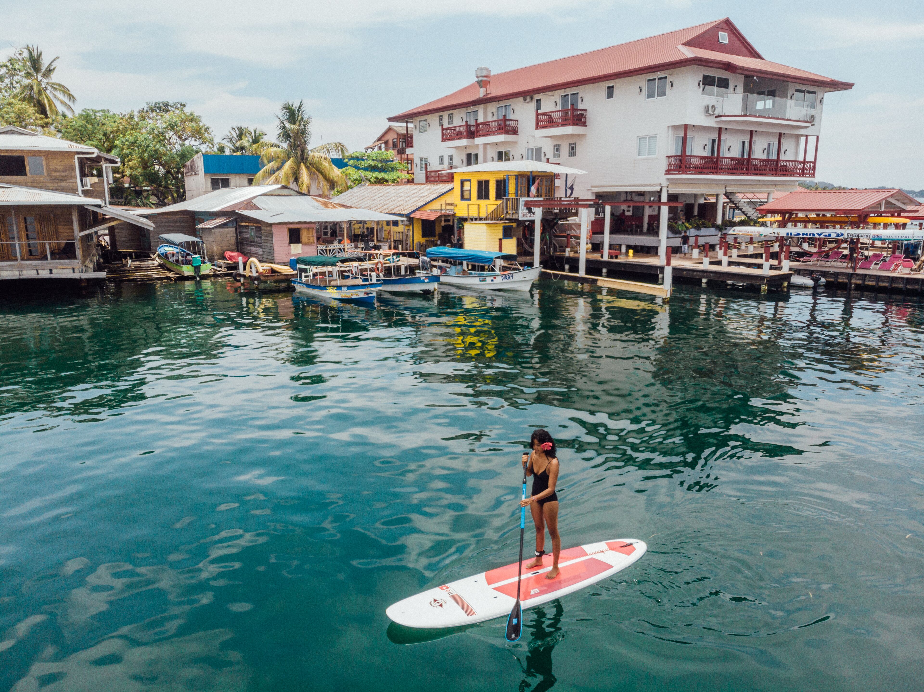 Zona costera con barcos amarrados, una persona haciendo paddleboard y edificios con balcones.