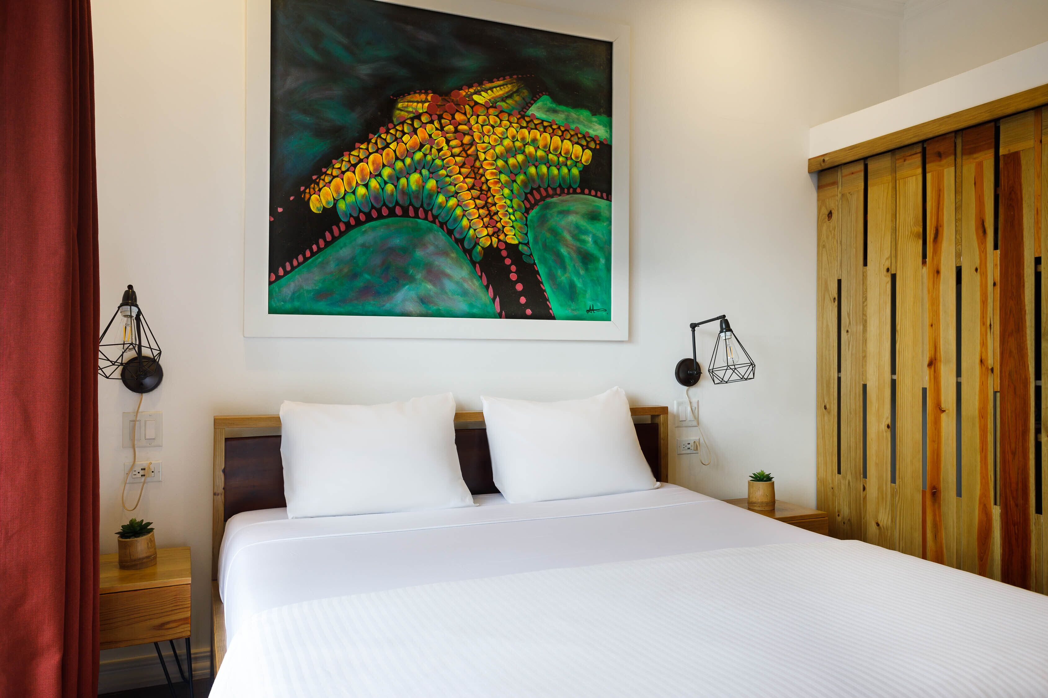 A neatly arranged hotel room with a large bed, a wooden wardrobe, a wall-mounted painting, and bedside lamps.