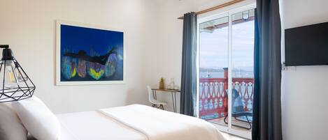 A bedroom with a bed, a ceiling fan, a window with curtains, a painting on the wall, and a balcony with a railing.