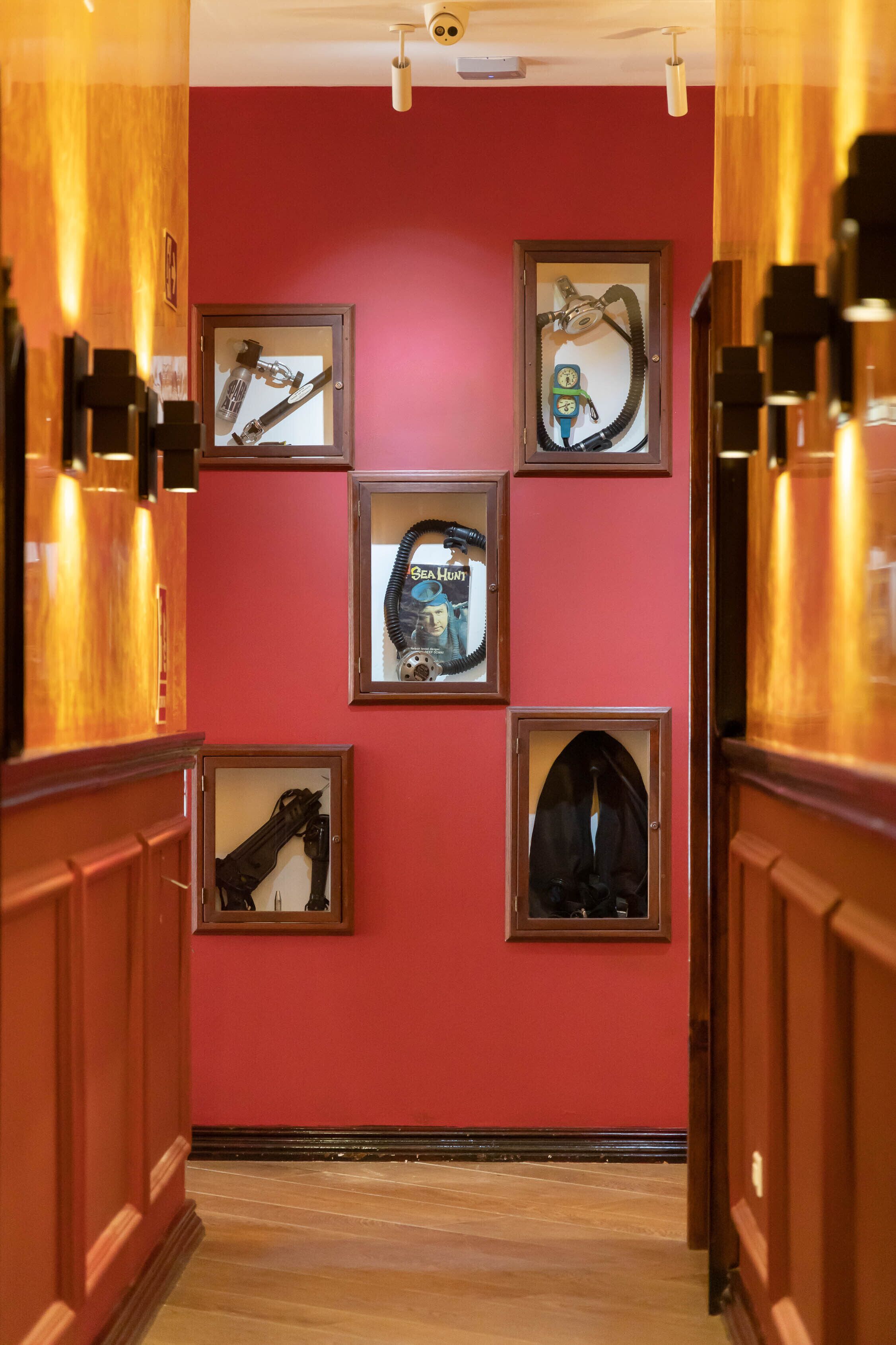 A hallway with wooden paneling and a red wall. There are framed pictures on the wall, including one with a clock and another with a guitar.