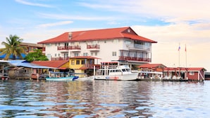 Um edifício à beira-mar com várias varandas, um cais com barcos e céu claro.